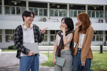 Students laughing and socializing outside on a college campus, one holding a laptop and chatting with friends