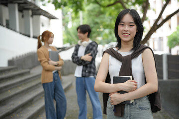 Joyful young woman student carries books on a college campus, enjoying the company of friends. Diverse students express youth and unity in a city setting, highlighting camaraderie and learning