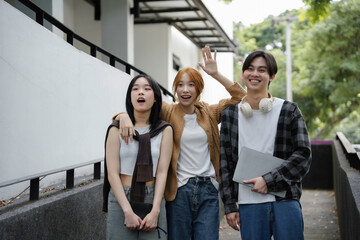 Three young people walking on a school campus, holding books and a laptop, excited for a new semester together