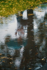 Person mit Regenschirm, die sich in einer Pfütze spiegelt