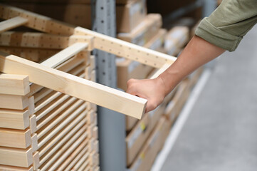 Hand of a person selecting a wooden item from a shelf in a warehouse, illustrating attention to detail. The scene captures a close-up view of the hand.