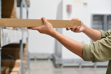 Hands holding a long cardboard box, focusing on proper storage in a warehouse environment.