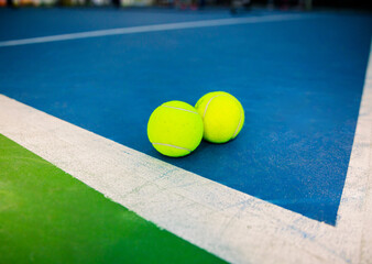 Two tennis balls on blue and green court. Close-up of two tennis balls on a blue and green court with white lines. The balls are bright yellow and placed near the corner.