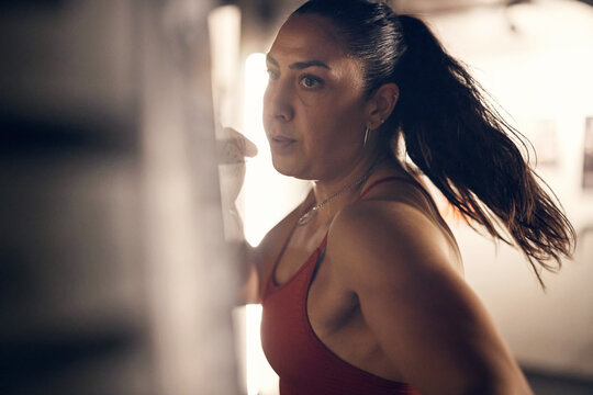 Fit young woman wearing a tank top and boxing gloves hitting a punching bag during boxing practice alone in a gym