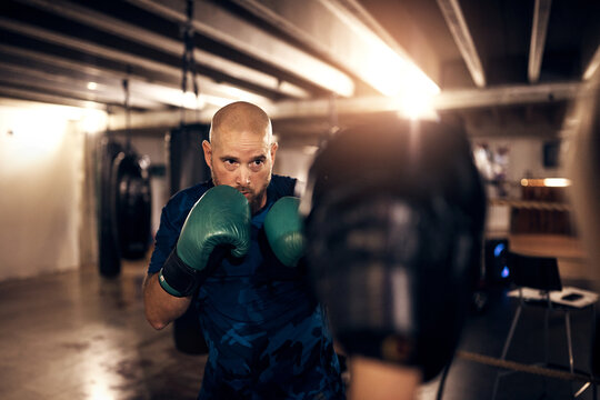 Mature man doing a punching workout in a boxing gym with a partner