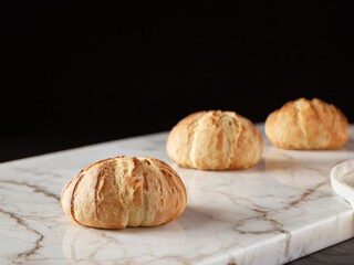 Fototapeta premium Three freshly baked bread rolls on a marble cutting board