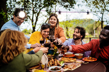 Diverse friends enjoying outdoor dinner party with wine and tapas under string lights, multicultural group celebrating in garden