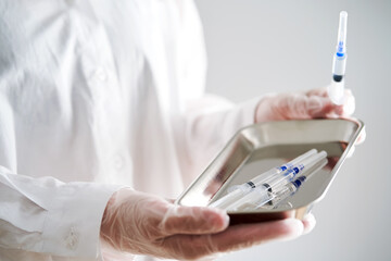 Anonymized photo of a doctor's hands holding a tray and a syringe with a needle.
