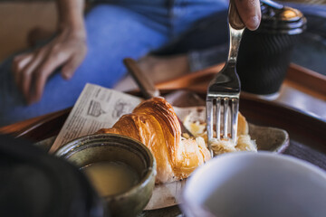 Part close up of woman is having a croissant and coffee.