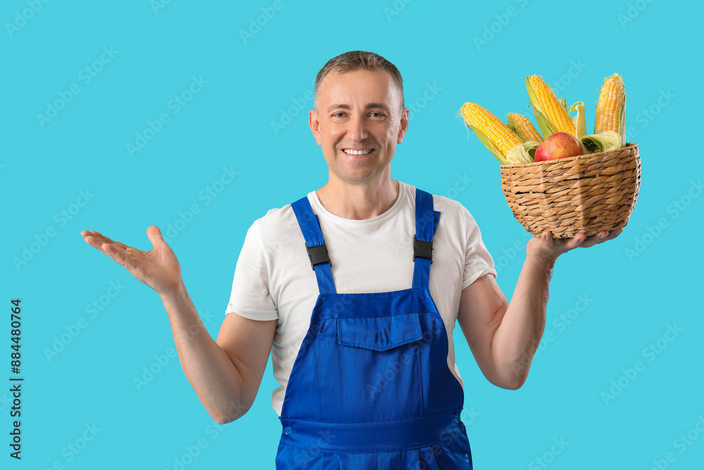 Canvas Prints mature male farmer with wicker basket full of corn cobs and apple on blue background