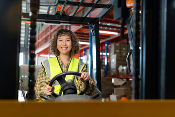 Cheerful female warehouse worker in a safety vest operates a forklift, showcasing a busy industrial environment.