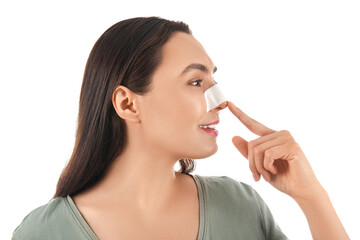 Young woman pointing at bandaged nose on white background. Plastic surgery concept
