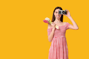 Obraz premium Happy smiling young woman with hyacinth flowers and camera on yellow background