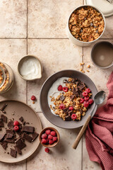 Granola with yogurt, chocolate, fresh raspberries and mint on beige tile background. Organic food for healthy and dieting breakfast, top view