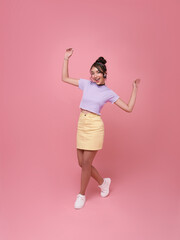 Happy Asian teen woman smiling and walking dance while celebrating success isolated on pink background.