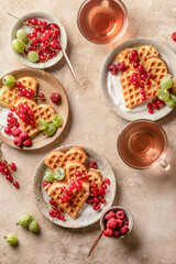 Homemade waffles with summer berries and yogurt served for sweet breakfast with tea on beige background. Heart shaped waffles top view