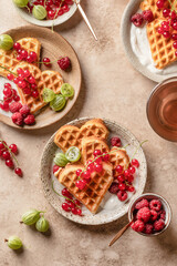 Homemade waffles with summer berries and yogurt served for sweet breakfast with tea on beige background close up. Heart shaped waffles top view