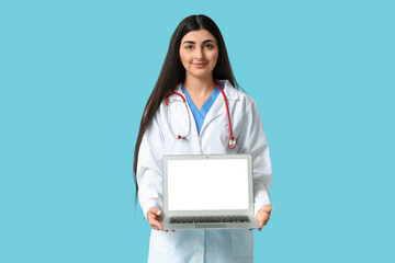 Beautiful young female doctor with stethoscope and laptop on blue background