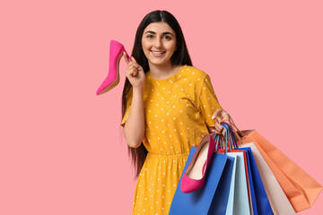 Happy smiling young woman with shopping bags and shoes on pink background