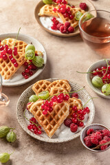 Homemade waffles with summer berries and yogurt served for sweet breakfast with tea on beige background. Heart shaped waffles