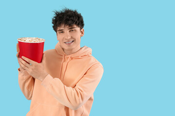 Young man with popcorn on blue background