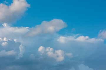 Obraz premium Scenic view to huge dramatic white clouds in blue sky. Nature background of fluffy cloudiness. Beautiful minimalist cloudscape. Nature texture of cloudy skies. Minimal skyscape in changeable weather.
