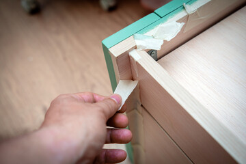 A person's hand removes painter's tape from furniture after repainting it in a different color