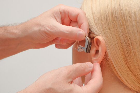 Doctor putting an hearing aid. The hands of a male audiologist trying on a hearing aid on a woman's ear. Helping technologies for people with disabilities