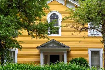Vibrant yellow house facade with arched window and lush green surroundings in Newton,...