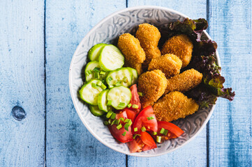 Close up of bowl with crispy nuggets, tomato and cucumber on the table top view