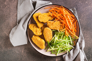Close up of chicken nuggets, grated cucumber and carrots on a plate on the table top view