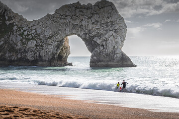 Two swimmers in waves near the Durdle Door, Dorset, UK