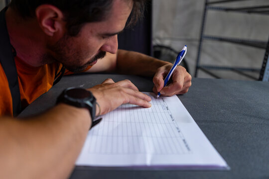 Man meticulously fills out a worksheet in a dimly lit room