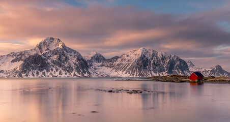 Serene dusk at Lofoten with red cabin and snowy mountains