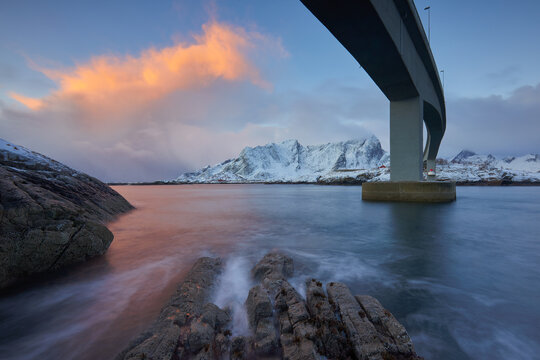 Dramatic sunset over snowy mountains and bridge in Lofoten