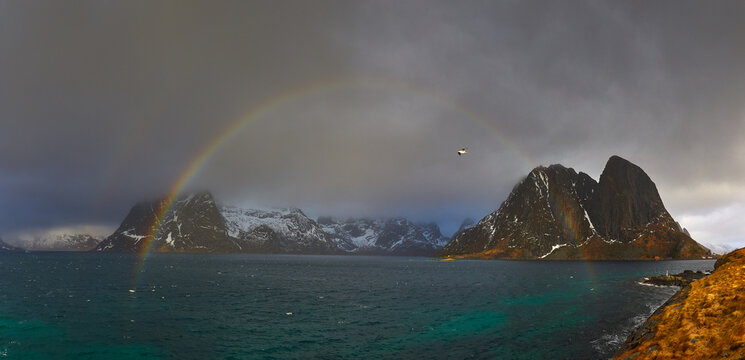 Dramatic rainbow over snow-capped mountains in Lofoten