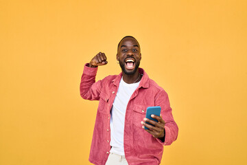 Happy Black man winner holding smartphone celebrating win isolated on yellow. Excited African young...