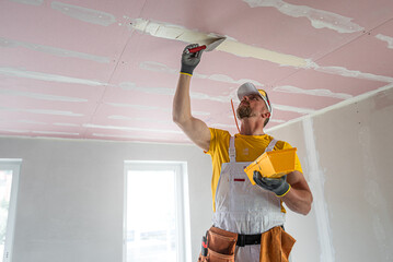The worker make a plasterboard ceiling. He does taping plaster drywall ceiling joints. A red...