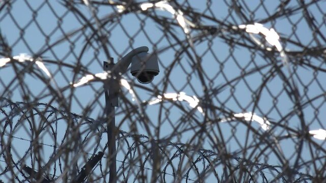 IOWA - 6.28.2024 - Close-up of a security camera seen through loops of barbed wire outside the Iowa State Penitentiary.