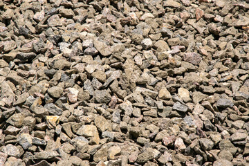 A close-up image of a pile of small, tan and gray gravel stones, illuminated by the sun