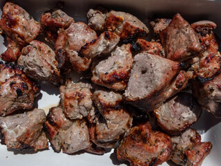 Macro of meat cooked on metal skewers - juicy pork grilled on fire, coals and smoke in grill. Seasoned cubes of meat