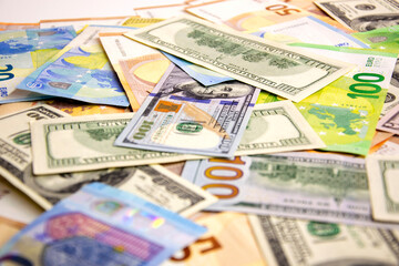 An assortment of US dollar and euro bills are scattered on a white surface