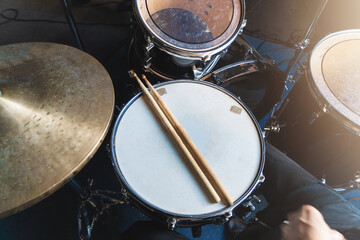 Drum kit with drumsticks placed on snare drum, illuminated by soft lighting in music studio, top...