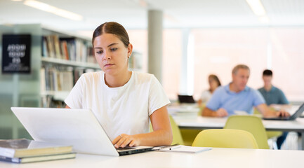 Fototapeta premium Young female European student studying with a laptop in the library
