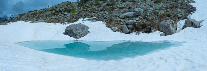 Thawing mountain lake with reflection of a stone