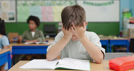 Education, exam and stress with boy student at desk in classroom for development. learning or study. Book, headache and scholarship with child reading at school for academy evaluation or knowledge - Powered by Adobe