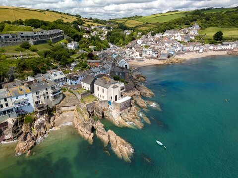 a coastal village with houses on cliffs and a beach, surrounded by green hills and a blue sea.
