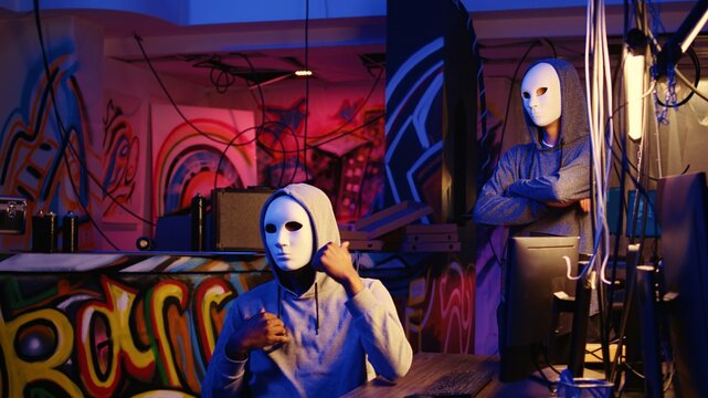 Hacker group members doing online terrorism acts, filming ransom video with smartphone in hidden underground base, threatening to release stolen sensitive data publicly if payout demands are not met