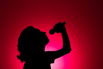 Silhouette of young man holding wireless microphone and singing music with emotion.