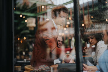 A business team engaged in a meeting in a modern cafe setting with reflections on the glass window and lights in the background.